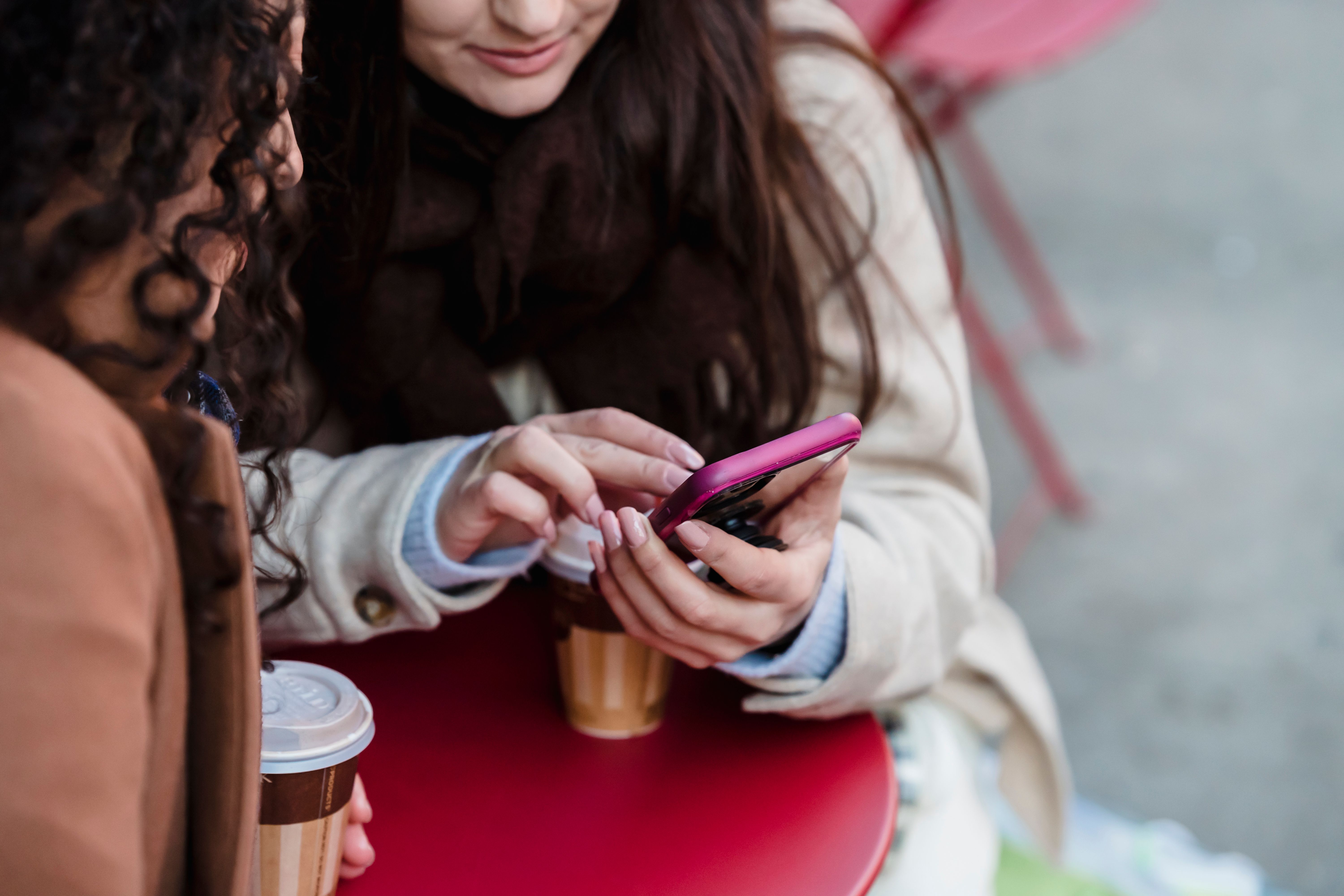 A close view of two friends sharing a phone over coffee, with the device and their hands in focus
